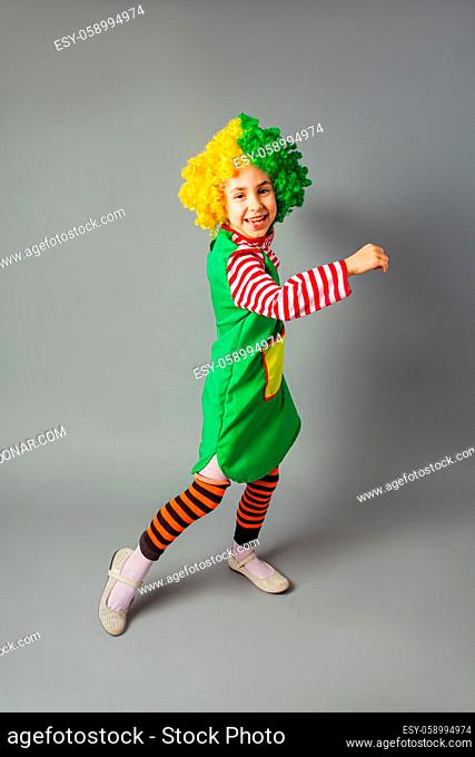 The little girl in a clown uniform has fun on a gray background. The girl is dancing and singing