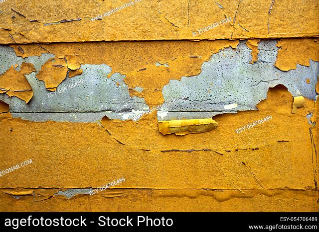 Concrete wall with yellow, orange peeling paint old cracked damaged rough bright background texture closeup
