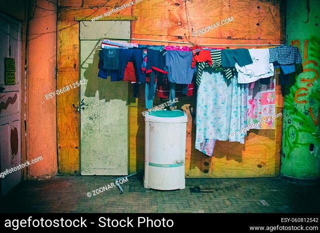 Washing machine and bed sheets and clothes hanged to dry on the outside of an apartment with worn wooden planks and cracked walls