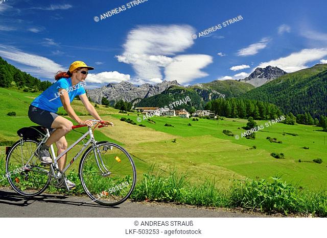Woman cycling along Inn cycle route, Bos-cha with Sesvenna Alps in background, Lower Engadin, Canton of Graubuenden, Switzerland