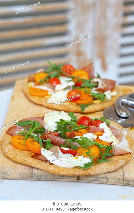 Pizzas topped with rocket, prosciutto, goat's cheese and tomatoes