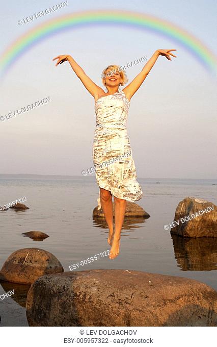 lovely blond jumping at the seashore under colorful rainbow