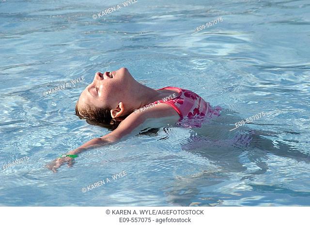 10-year-old girl in swimming pool, face up to sun, back curved, between standing and floating, wearing pink-and-white swimsuit -- Bloomington, Indiana, U