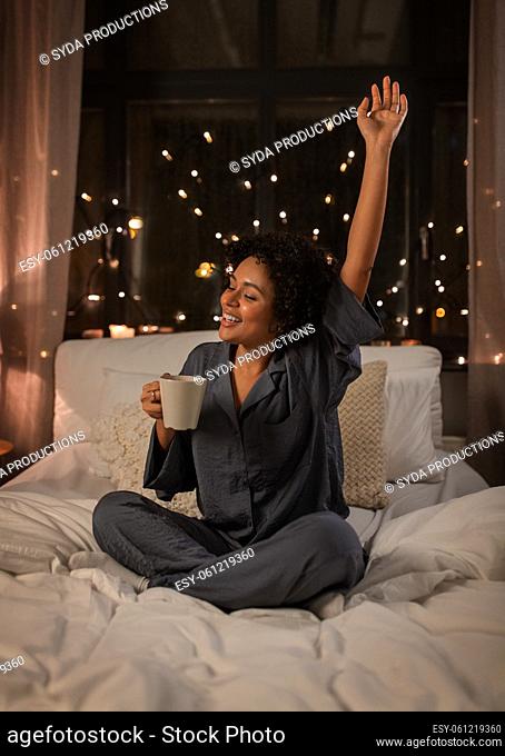 happy woman with coffee stretching in bed at night