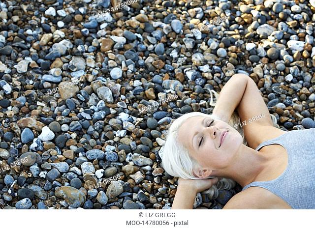Young woman smiling lying on pebble beach elevated view