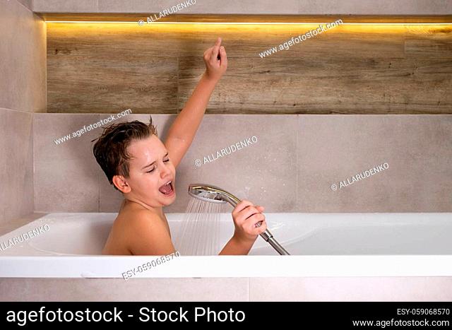 Happy boy holding shower head and singing while washing in bathroom Child bathe at home healthy childhood