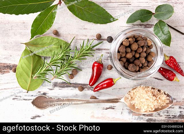 Bay leaves, traditional spice and condiment on white wooden background. Bay leaves, rosemary, chillies and black pepper on white wooden table, top view