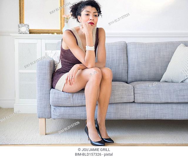 Mixed race woman in cocktail dress sitting on sofa