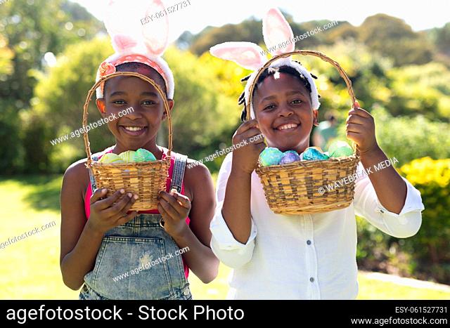 Happy african american brother and sister in bunny ears holding baskets of easter eggs
