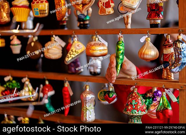 21 November 2023, Bavaria, Nuremberg: A stand operator places Christmas tree decorations for sale at her stand during the set-up work at the Nuremberg Christmas...