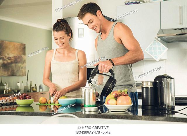 Young couple preparing a coffee and fruit breakfast at kitchen counter