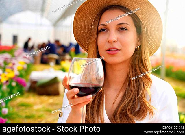 Image of cute young woman enjoying sitting outdors in park holding glass drinking wine