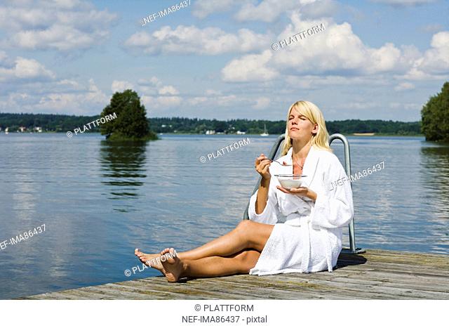 Woman sitting and eating breakfast on jetty