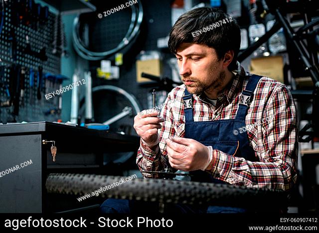 Technical expertise taking care bicycle shop. Handsome young mechanic fixing cycle wheel in workshop. Handsome repairman in workwear serving mountain bicycle