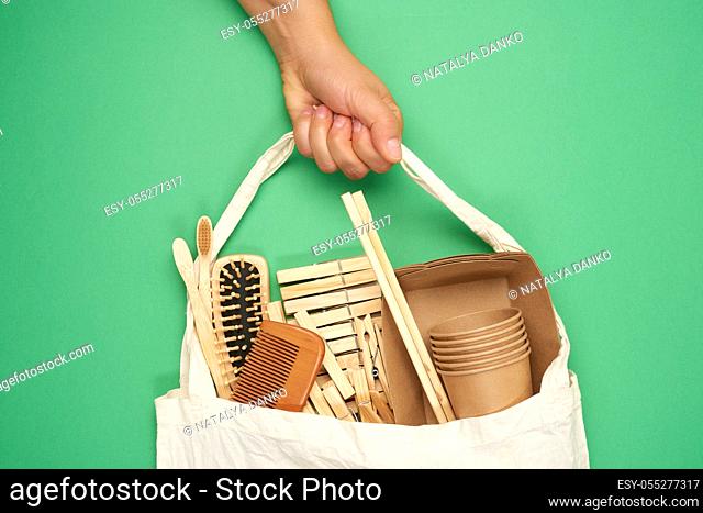 female hand holds full textile bag of recyclable household items, green background, zero waste