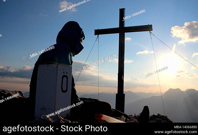 young woman at rest, mountain cross in sunrise, border stone germany, austria, hike, obere wettersteinspitze, 2.297m germany, bavaria, upper bavaria