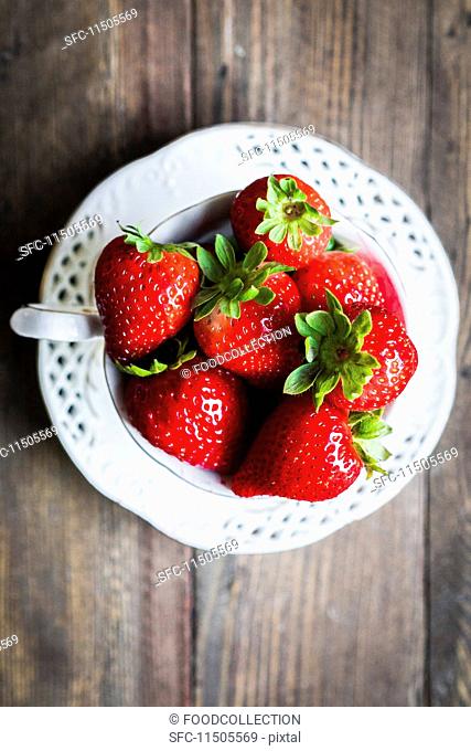 Fresh strawberries in a teacup on a wooden table