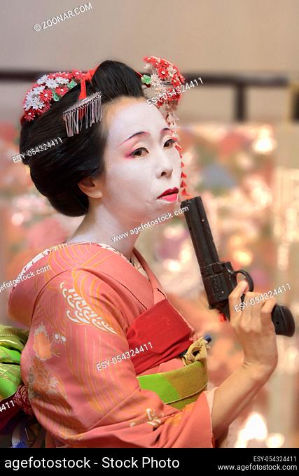 Pretty young Geisha maiko girl in kimono holding a plastic gun in her hand