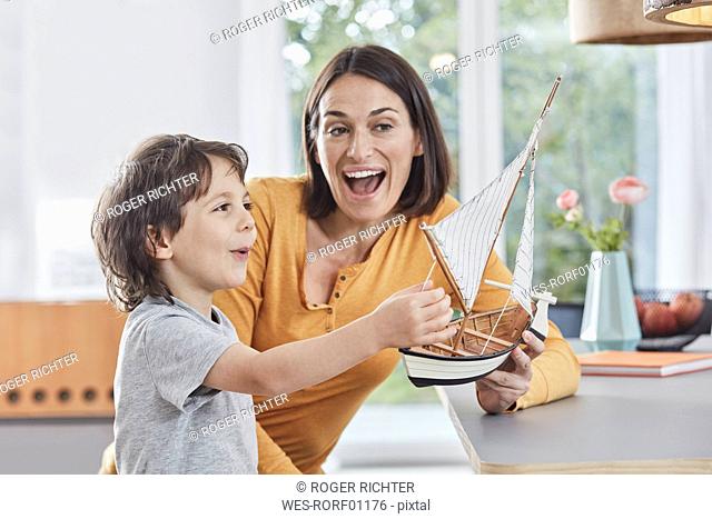 Happy mother and son playing with model boat at home