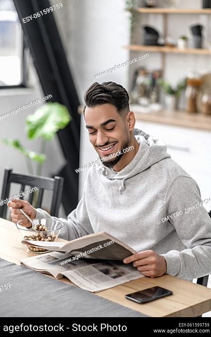 Morning news. A young man having breakfast and reading a newspaper