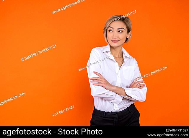 Confident woman wearing white official style shirt standing with crossed arms looking away isolated over orange background