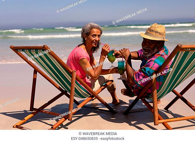 Senior couple relaxing on sun lounger and drinking cocktail on beach