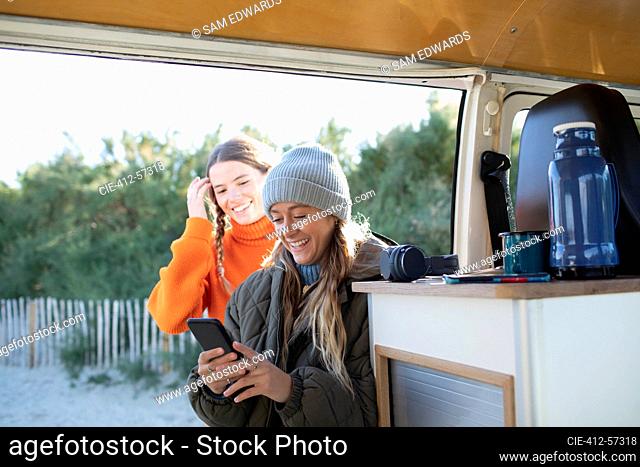 Young women friends using smart phone in camper van doorway