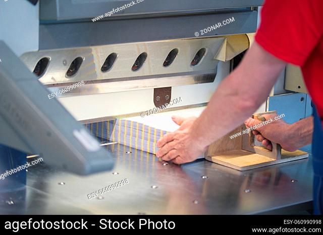 Hands of worker working on cutter guillotine machine in a printing factory, close up