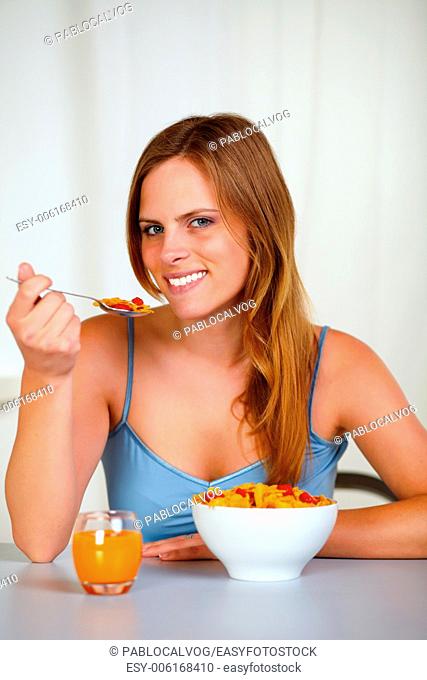 Closeup portrait of a relaxed pretty young girl eating cereals and strawberry for breakfast at home