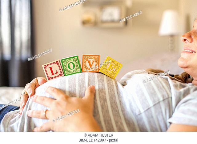 Pregnant Caucasian woman balancing wooden blocks on her stomach in bed