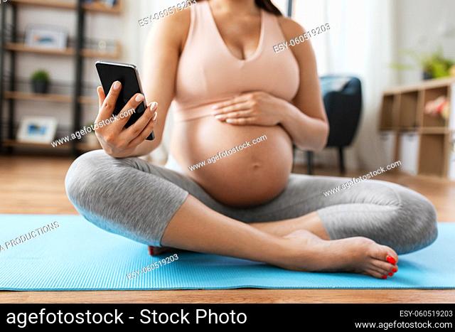 close up of pregnant woman with phone on yoga mat