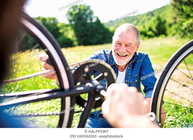 A senior father and his unrecognizable father repairing bicycle outside on a sunny day