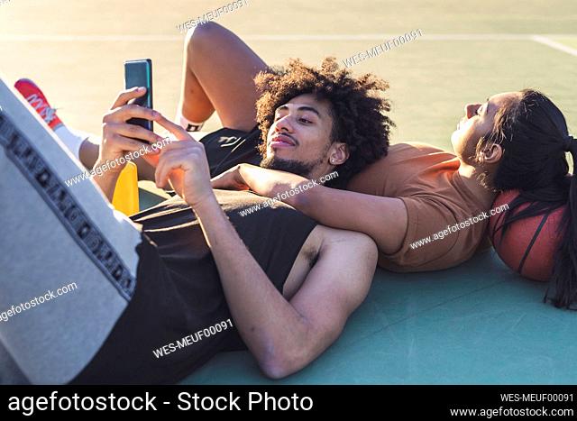 Sportive young couple taking a break lying on basketball court