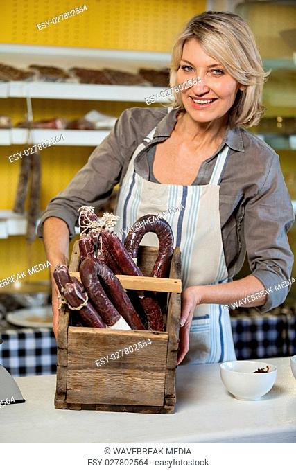 Portrait of female staff holding sausage in wooden basket at counter