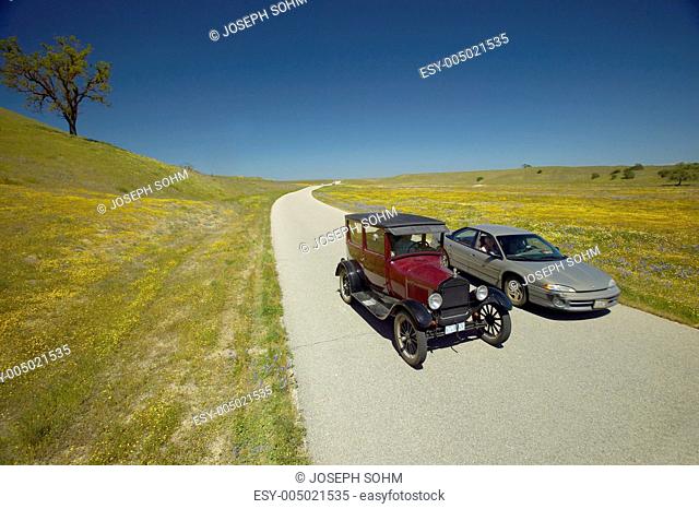 A modern car driving by a maroon Model T on a scenic road surrounded by spring flowers off of Route 58, Shell Road, CA