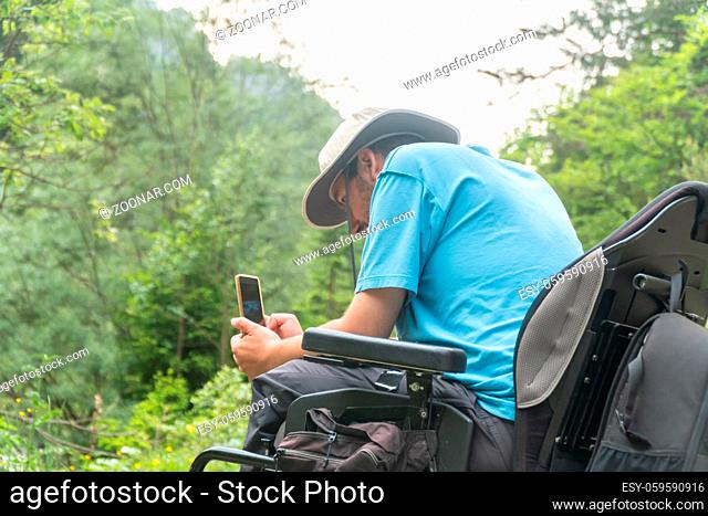 man on wheelchair using smartphone camera in nature