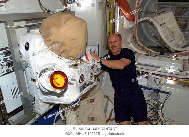 Astronaut Kenneth D. Bowersox, Expedition Six mission commander, is pictured near the torso portion of an Extravehicular Mobility Unit (EMU) spacesuit stored in...