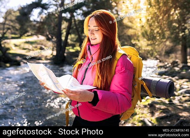 Smiling woman wearing backpack reading map standing in forest