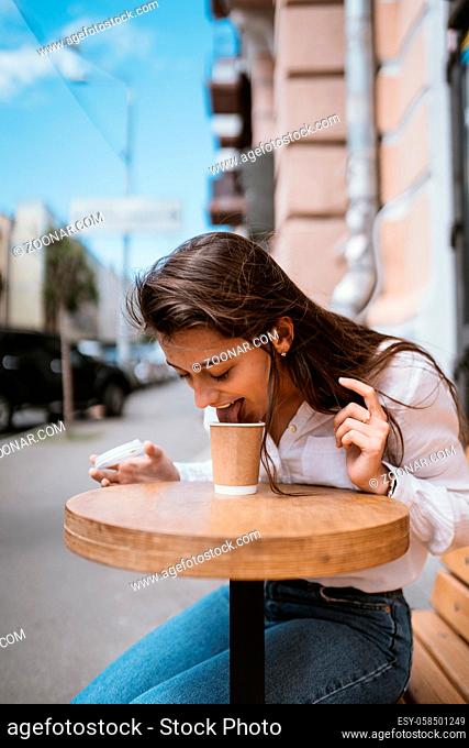 Beautiful young woman in street cafe drinks coffee, outdoor