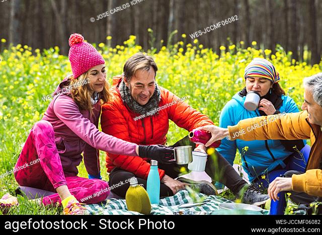 Mature man pouring coffee to woman sitting with friends in forest