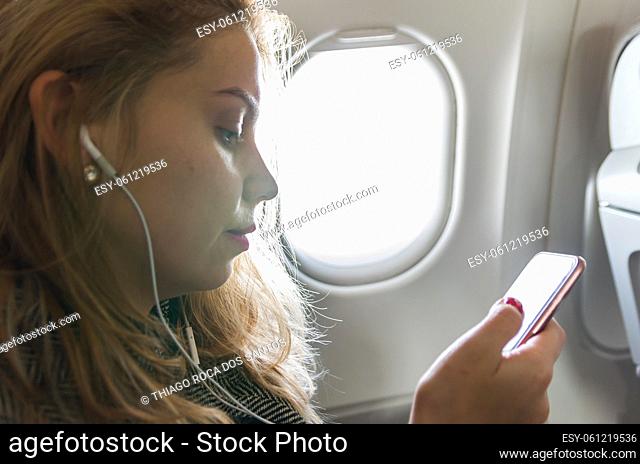 Young blond woman using smartphone on airplane
