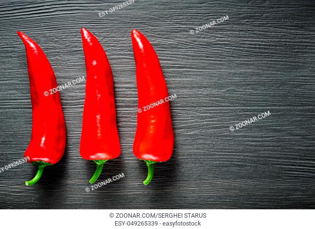Three ripe sweet red Kapia peppers on dark shale stone background, copy space