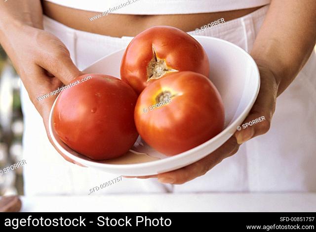 Young woman holding bowl with three tomatoes