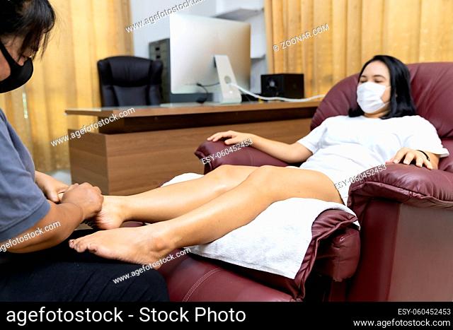 Quarantine asian woman do foot massage at home with face mask while city lockdown for social distance due to coronavirus pandemic