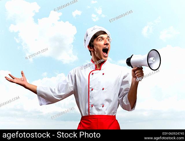 Young chef shouting loudly into megaphone. Emotional caucasian chef in white hat and red apron on blue sky background. Restaurant advertisement