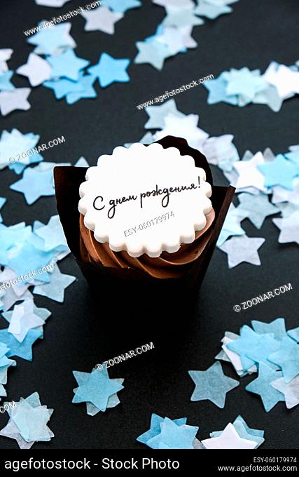 Happy birthday written in Russian on Delicious chocolate cupcake with cream on dark background. Muffin. Birthday cake party