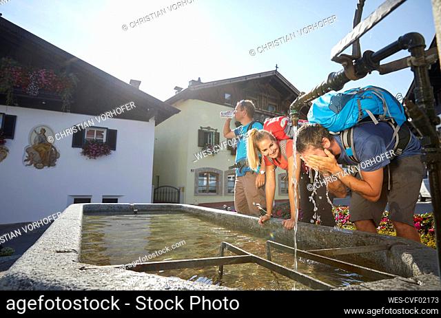 Hiker washing face by friends at fountain in village on sunny day, Mutters, Tyrol, Austria