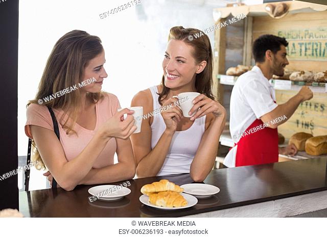 Women drinking coffee with barista in background at coffee shop