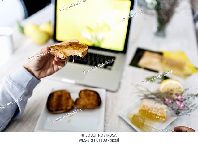Man's hand holding bitten toast with dripping honey at his workplace, close-up