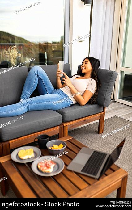 Happy young woman using smart phone on sofa in living room